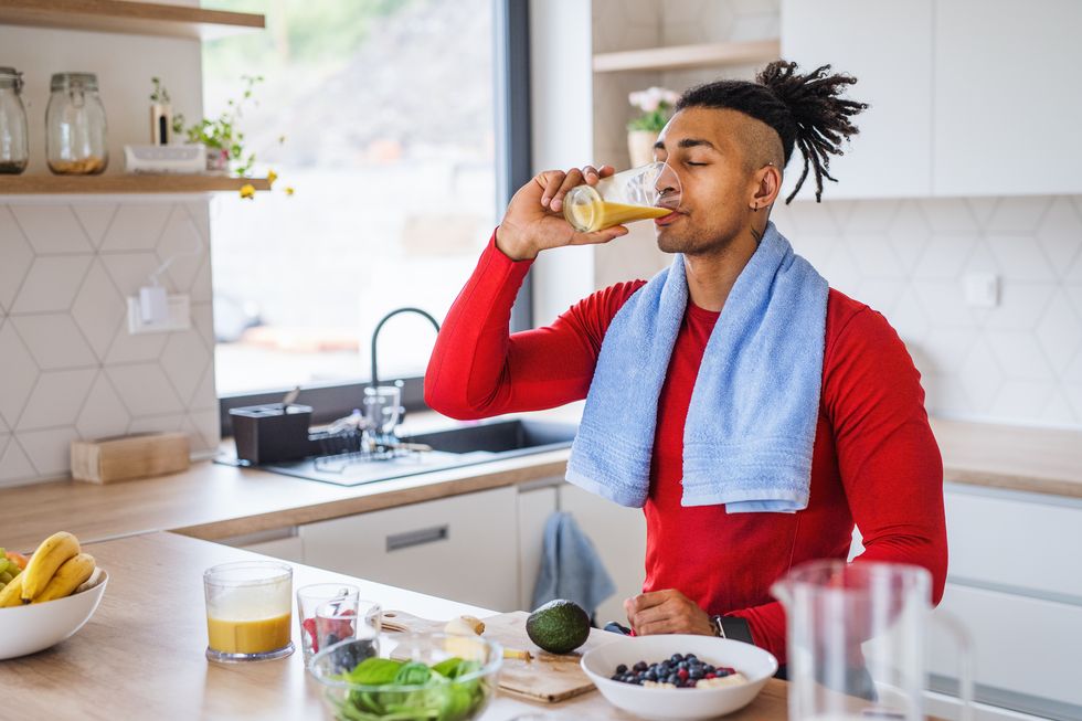 image of healthy mixed race man resting after exercising at home and drinking juice